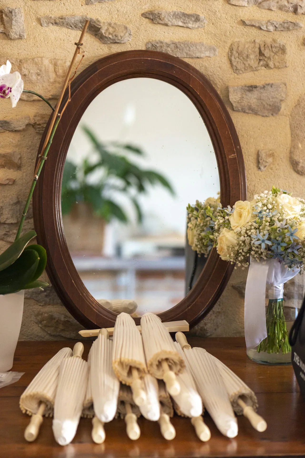 Un bouquet de fleurs et des ombrelles blanches posés devant un miroir ancien