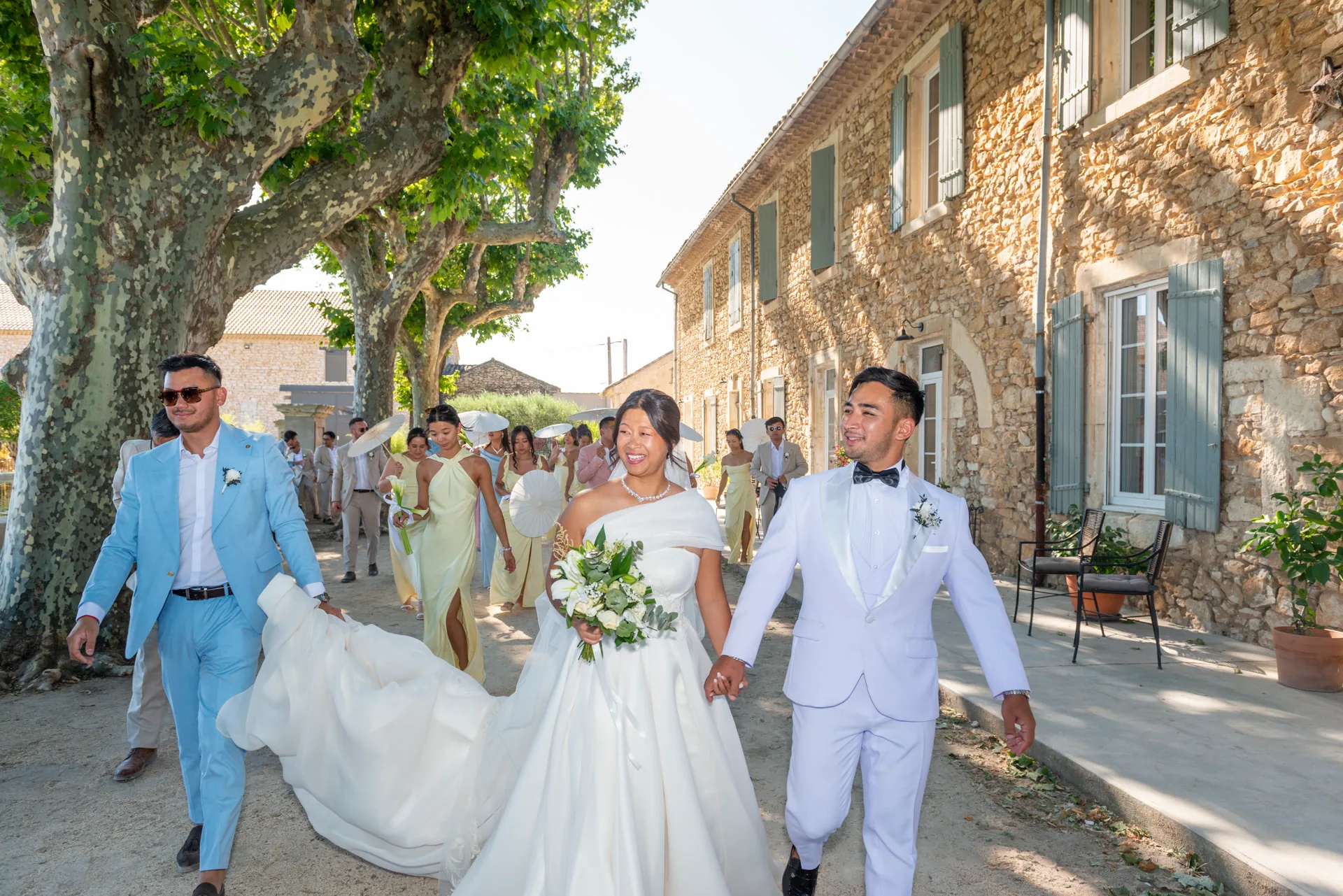 Le cortège des mariés et invités avance dans une allée bordée d'arbres