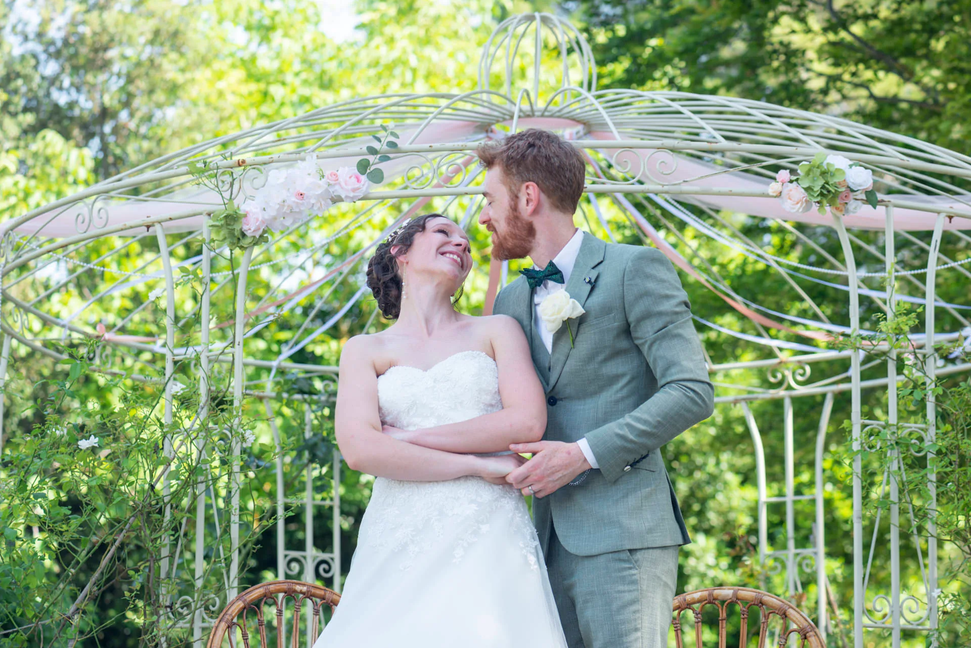 Un couple de mariés échange un regard sous un kiosque décoré de fleurs
