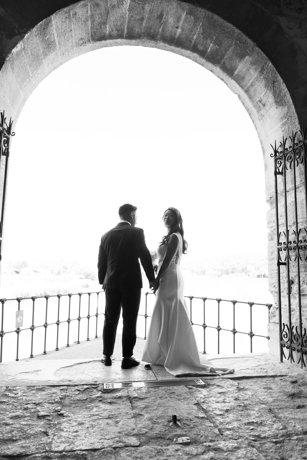 Les mariés se tiennent la main sous une grande arche en pierre, lors d'un mariage en Provence