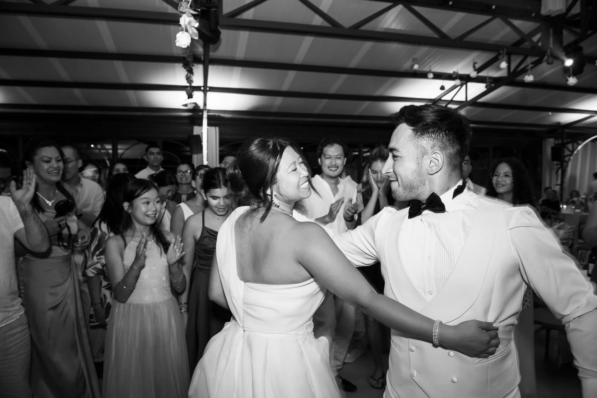 Les mariés dansent enlacés devant leurs invités, en noir et blanc