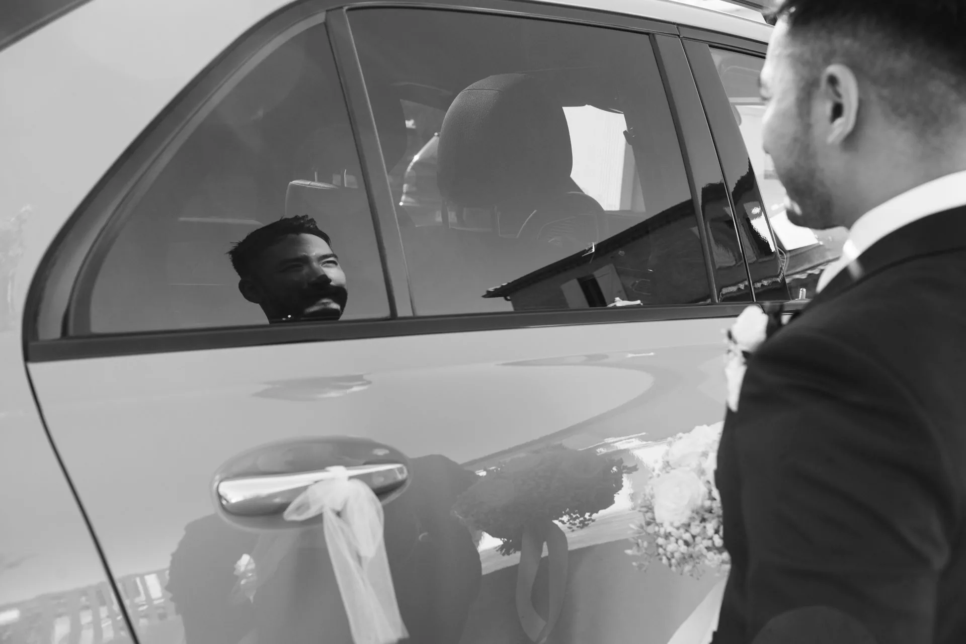 Le marié échange quelques mots à la portière de la voiture ornée d'un ruban, en noir et blanc