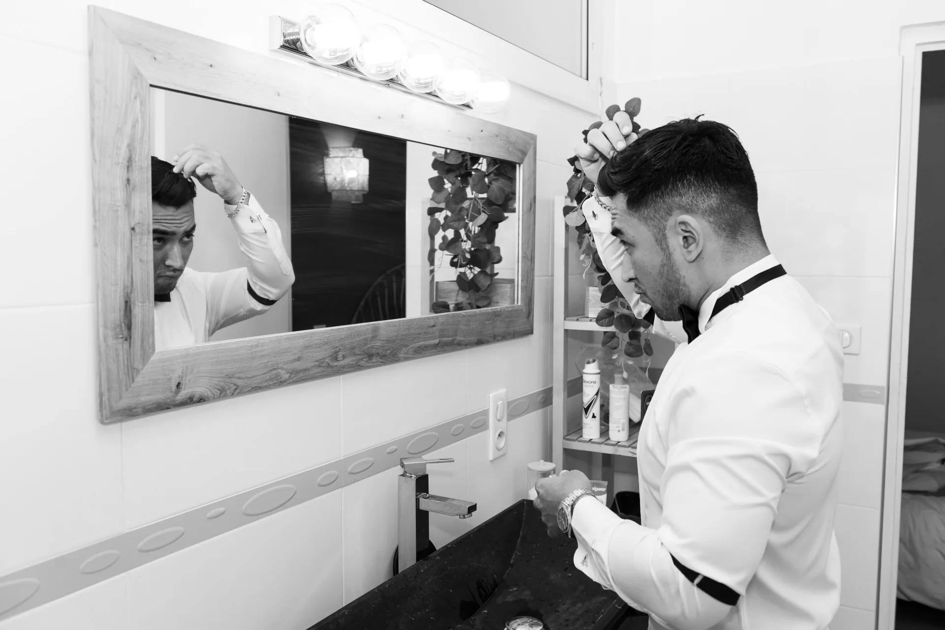 Le marié se coiffe devant le miroir de la salle de bain, en noir et blanc