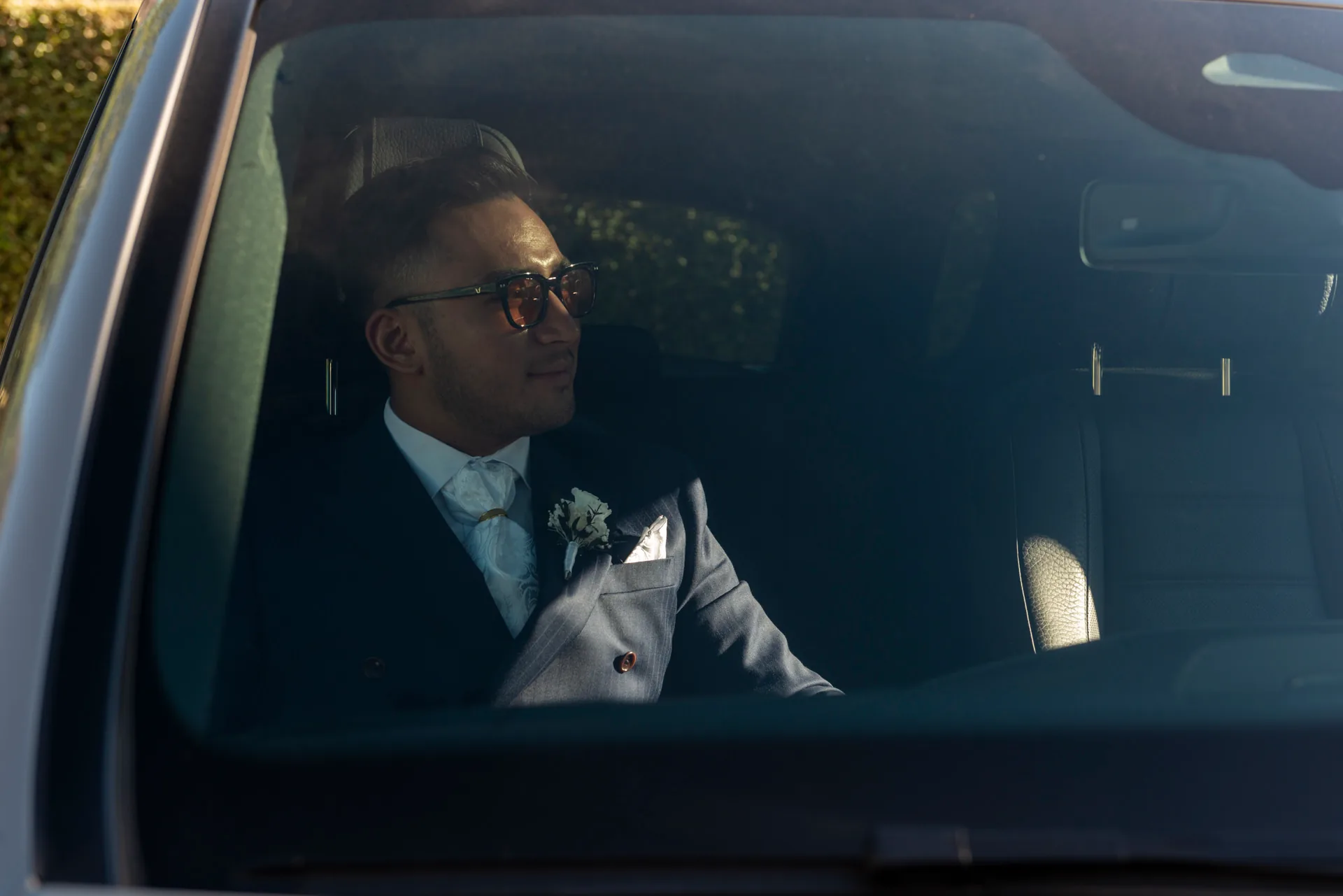 Le marié, lunettes de soleil et fleur à la boutonnière, patiente dans la voiture avant la cérémonie