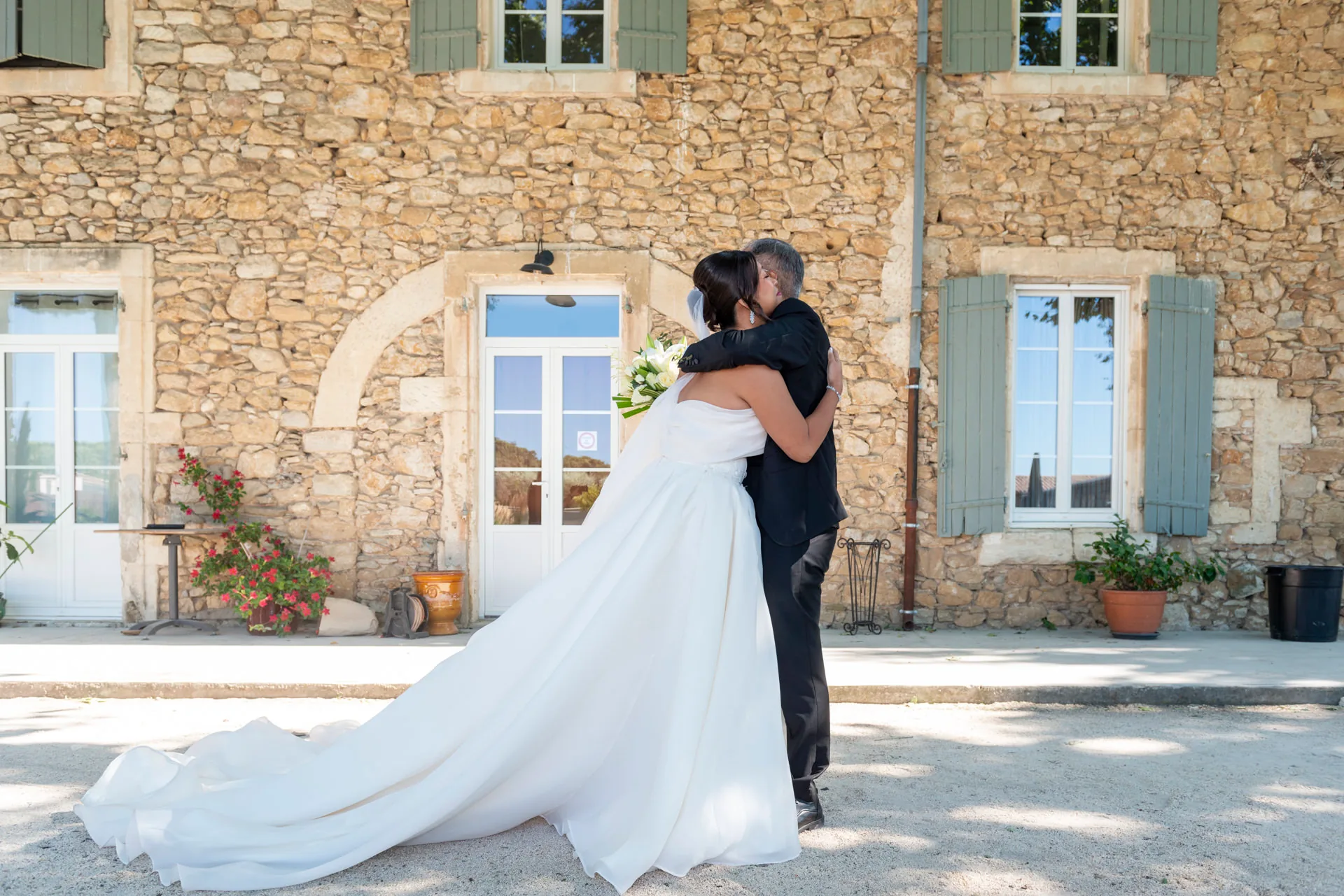La mariée enlace son père devant la façade du domaine