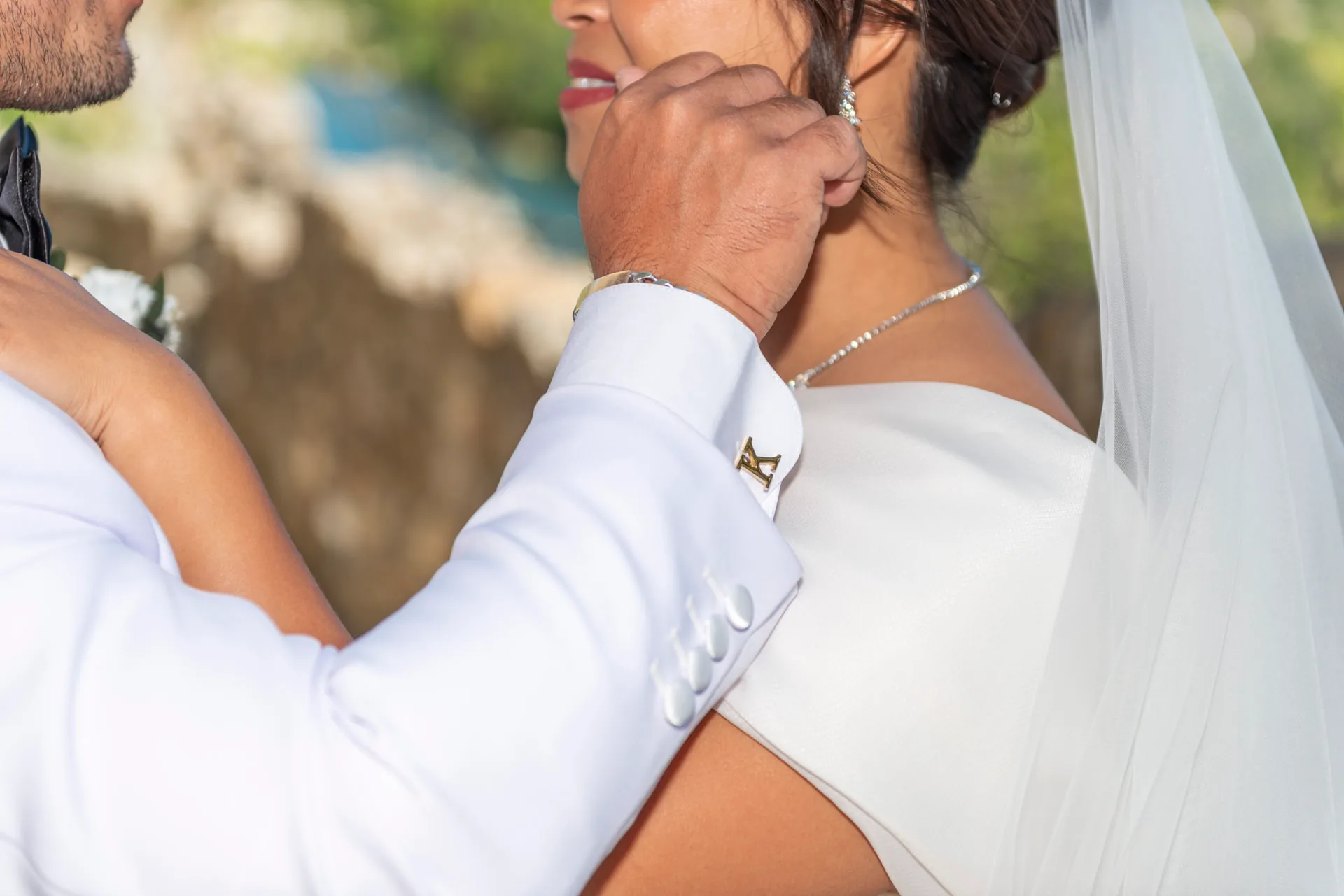 Le marié caresse le visage de la mariée, détail des bijoux et boutons de manchette