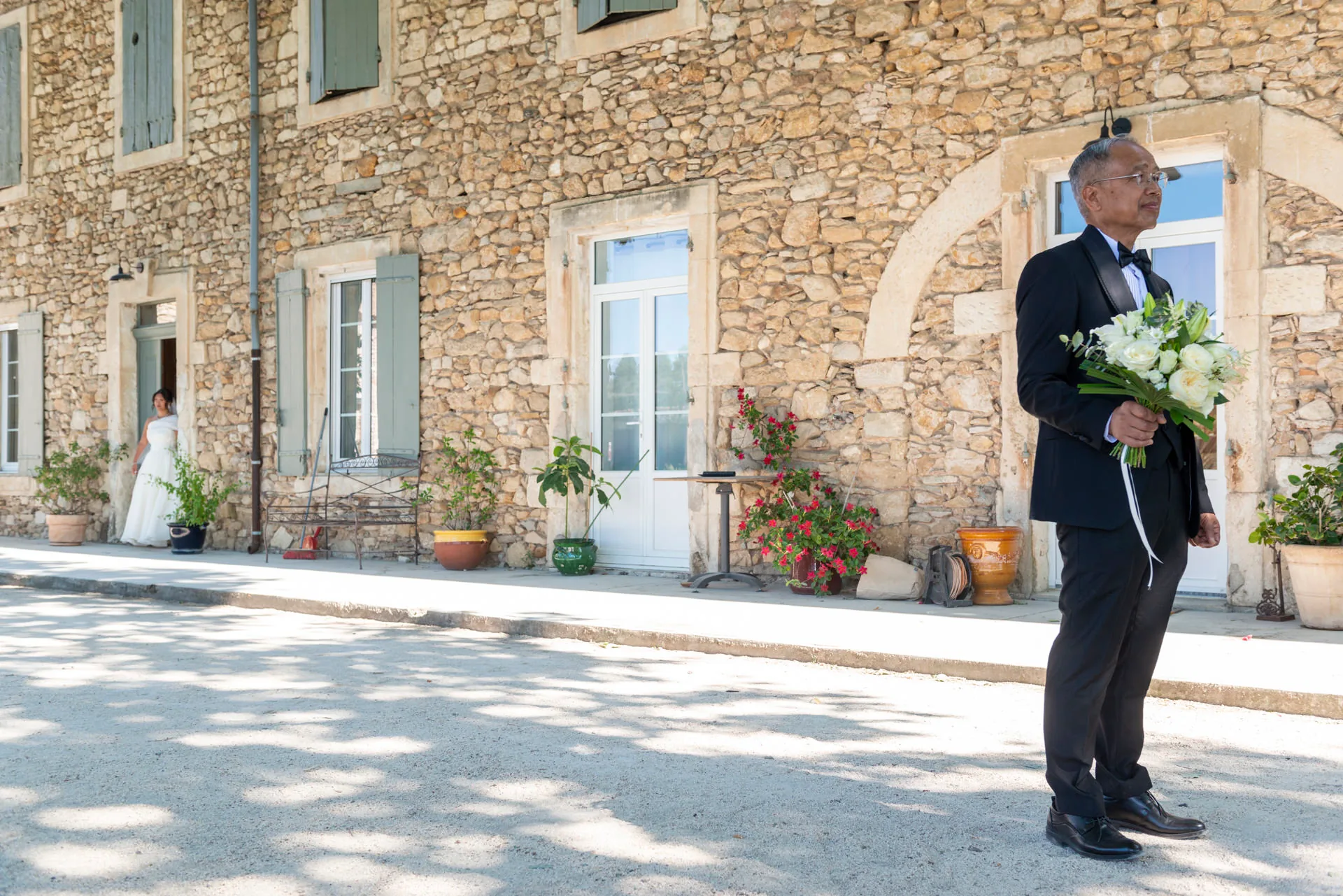 Le père de la mariée patiente avec le bouquet devant le domaine en pierre